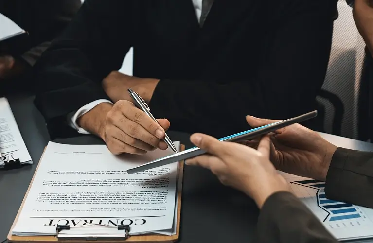 Business professionals seated at a table, reviewing documents with pens in hand