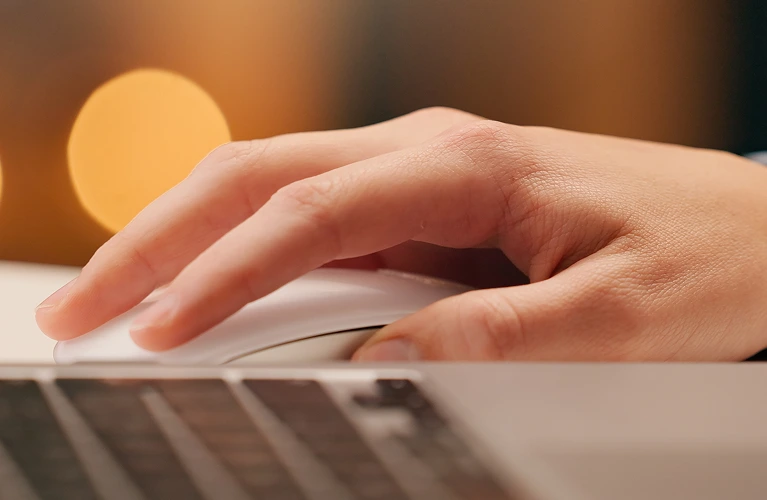A person's hand rests on a laptop mouse, ready to navigate the computer screen
