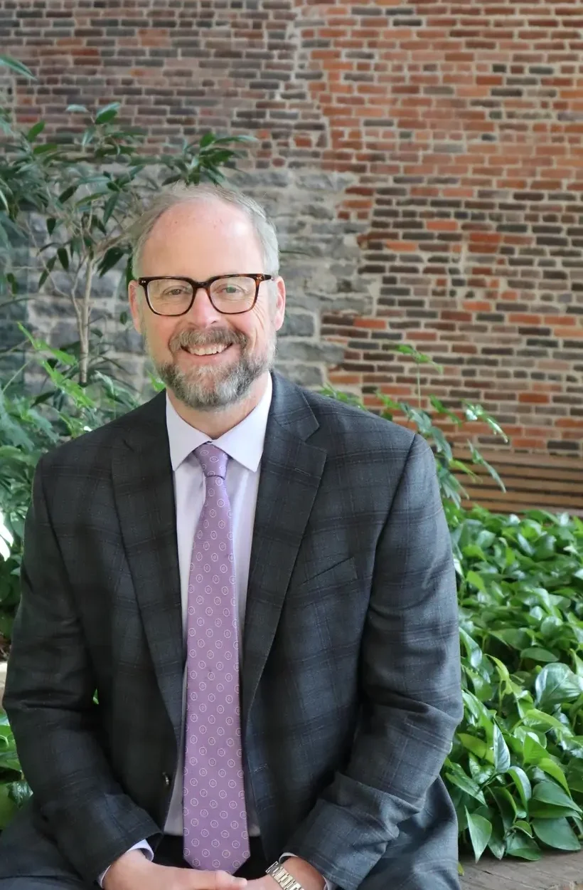 Eric Herbert, a man with glasses, wearing a purple tie, poses for the camera