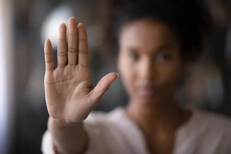 Close-up of a raised hand in focus with a blurred young woman in the background.