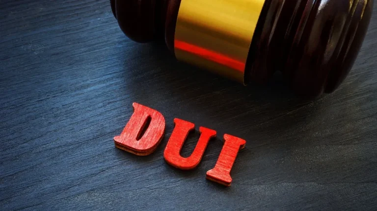 Close-up of a wooden judge's gavel next to red letters spelling "DUI" on a dark surface.