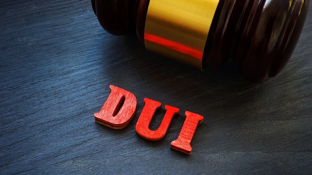 Close-up of a wooden judge's gavel next to red letters spelling "DUI" on a dark surface.