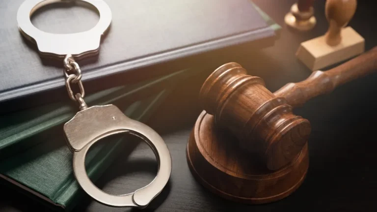 Wooden judge's gavel, metal handcuffs, and stacked law books on a dark surface.