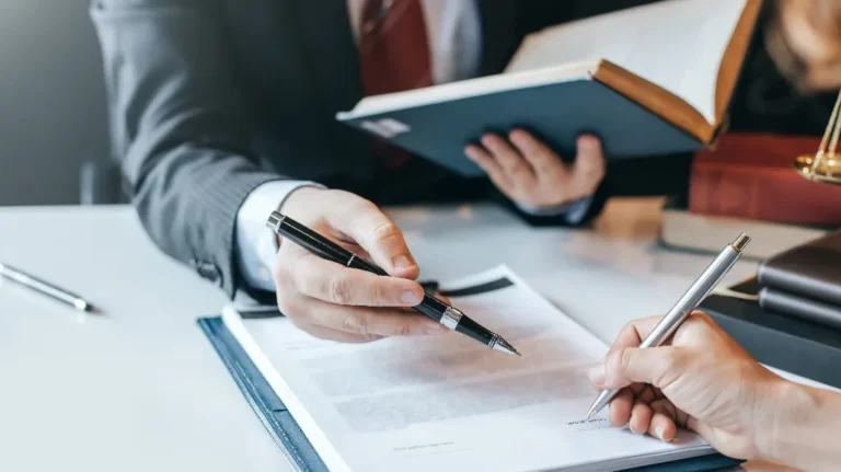 Two professionals in business attire reviewing and signing a document at a desk.