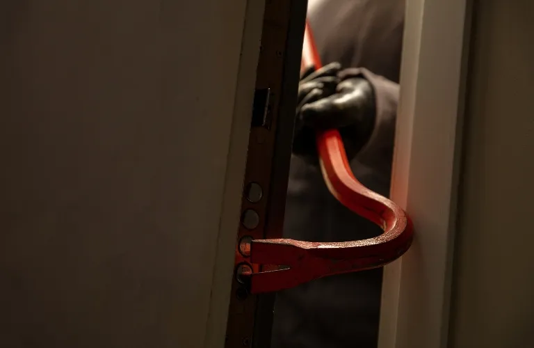 Person wearing black gloves holding a red crowbar prying open a door.