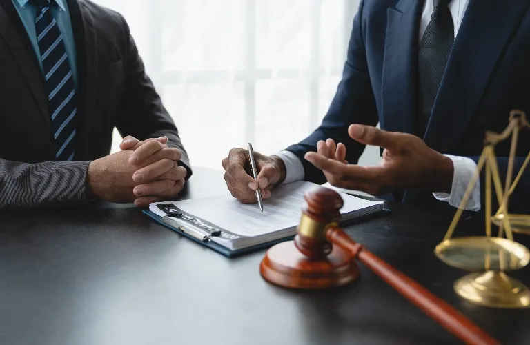 Two men in suits discussing legal documents with gavel and scales of justice on table.