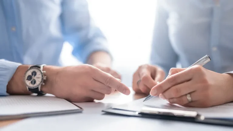 Two people in blue shirts reviewing and signing documents on a white table.