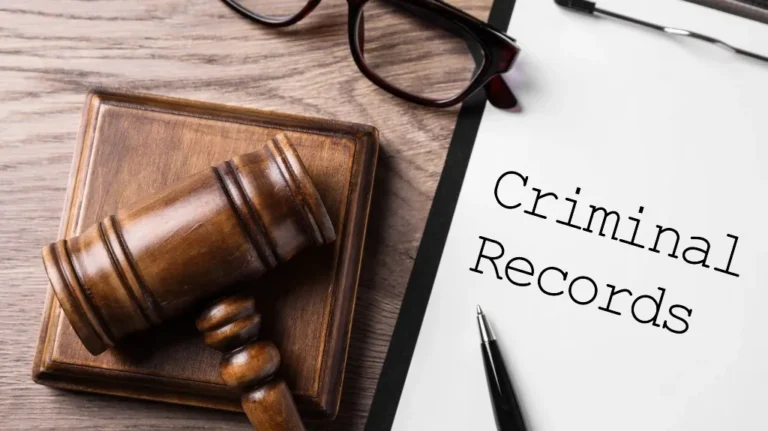 Wooden judge gavel on block beside glasses and paper labeled "Criminal Records" with pen.