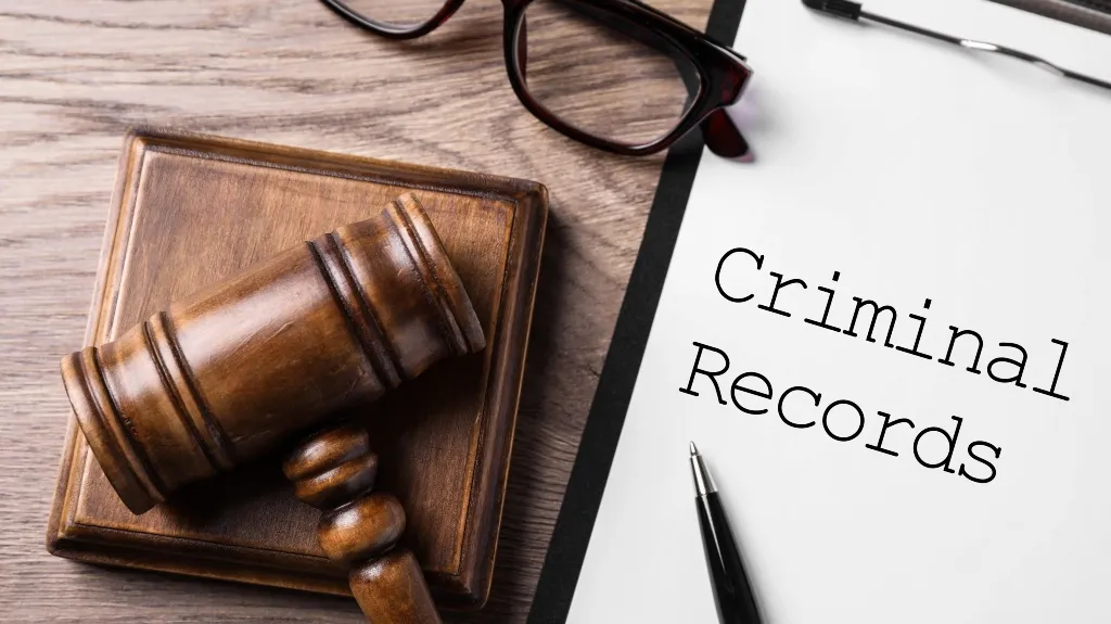 Wooden judge gavel on block beside glasses and paper labeled "Criminal Records" with pen.