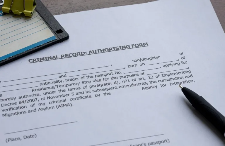 Close-up of a criminal record authorising form with a black pen and yellow binder clip on a wooden surface.
