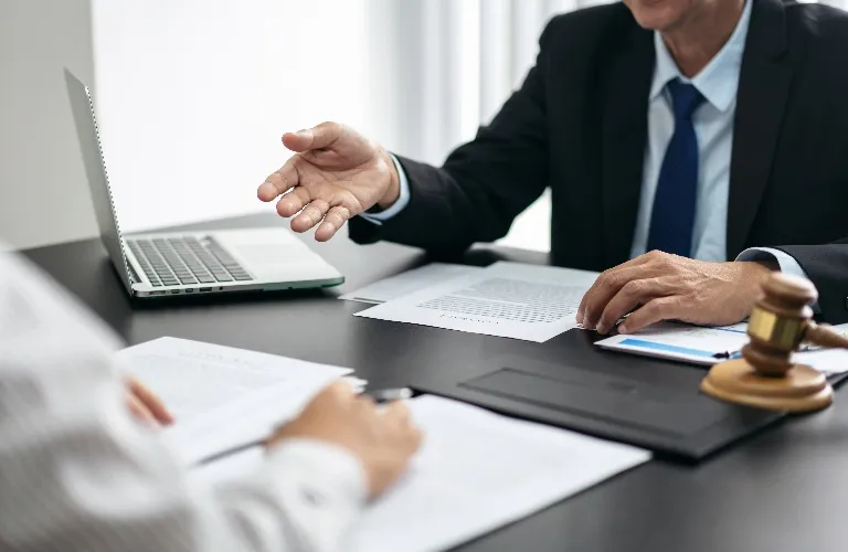 Two professionals in a formal meeting with documents, a laptop, and a judge's gavel on the table.