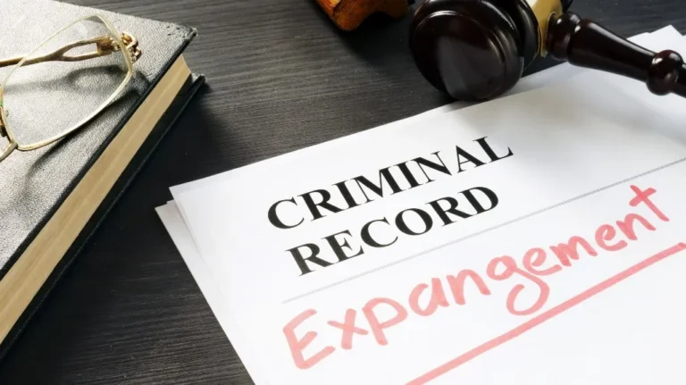 Document labeled "Criminal Record" with "Expungement" handwritten in red, next to a gavel and eyeglasses on a dark wooden surface.