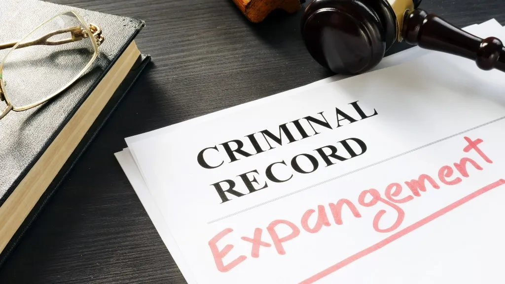 Document labeled "Criminal Record" with "Expungement" handwritten in red, next to a gavel and eyeglasses on a dark wooden surface.