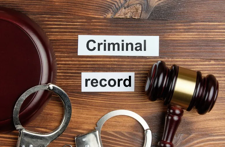 Wooden surface with judge's gavel, handcuffs, and paper labels reading "Criminal record".