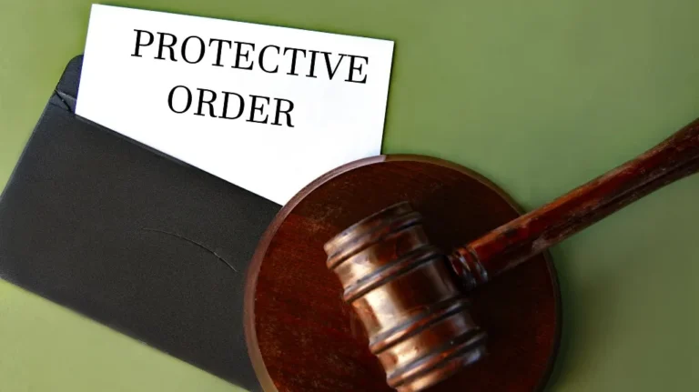 Wooden judge's gavel resting on a block next to a black envelope labeled "Protective Order.