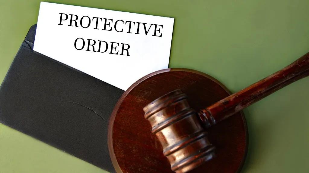 Wooden judge's gavel resting on a block next to a black envelope labeled "Protective Order.