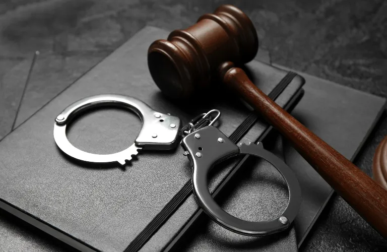 Wooden judge's gavel and metal handcuffs resting on black hardcover books.