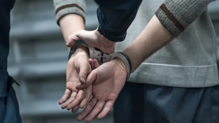 Close-up of a person in handcuffs being restrained by another individual.