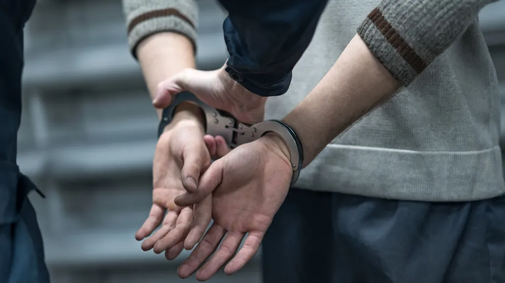 Close-up of a person in handcuffs being restrained by another individual.