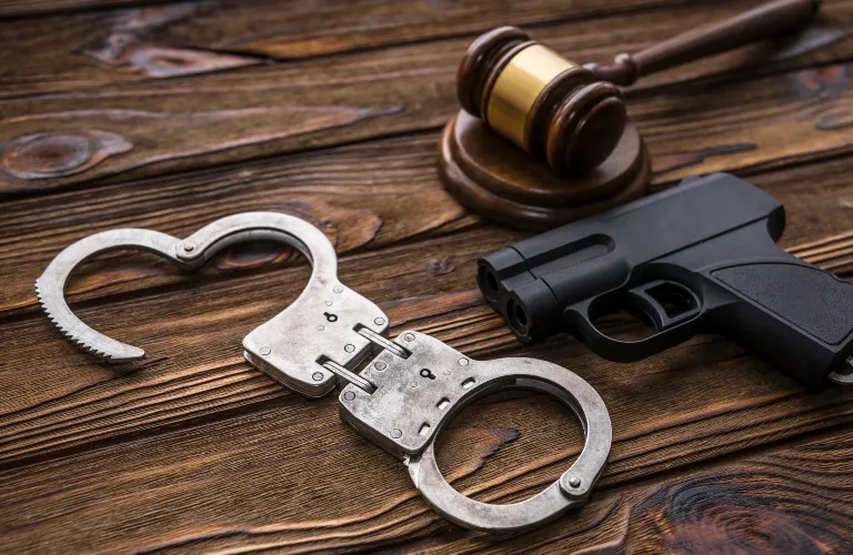 Metal handcuffs, a black handgun, and a wooden judge's gavel on a wooden surface.