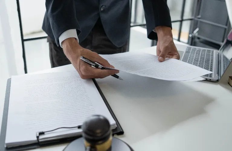 Person in dark suit reviewing documents at a white desk with laptop and gavel.